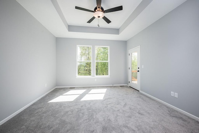 carpeted empty room featuring ceiling fan, a tray ceiling, and baseboards