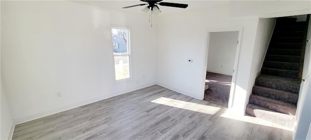 unfurnished room with baseboards, a ceiling fan, wood finished floors, and stairs