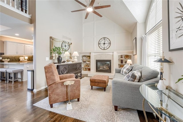 living room with ceiling fan, dark hardwood / wood-style floors, high vaulted ceiling, and a tile fireplace