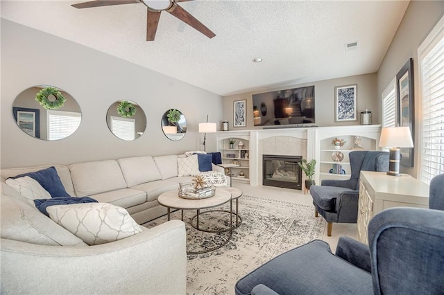 living room with ceiling fan, plenty of natural light, a fireplace, and a textured ceiling