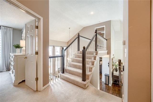 stairway featuring lofted ceiling, carpet flooring, and a textured ceiling