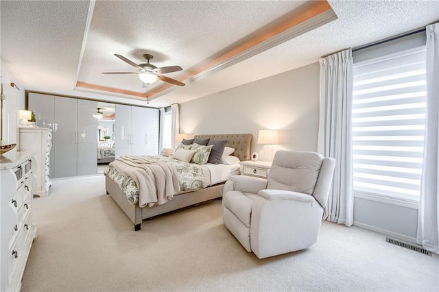 bedroom featuring ceiling fan, a raised ceiling, light carpet, and a textured ceiling