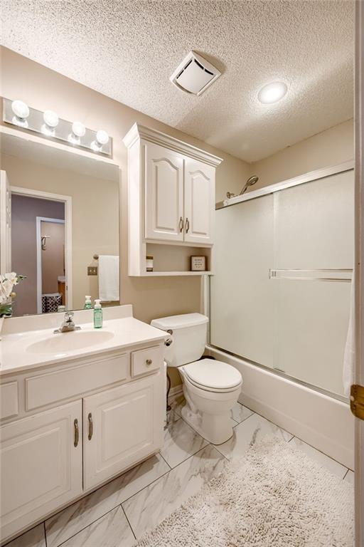 full bathroom with vanity, toilet, shower / bath combination with glass door, and a textured ceiling