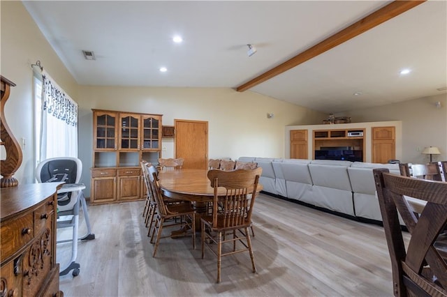 dining space with light wood-type flooring and vaulted ceiling with beams