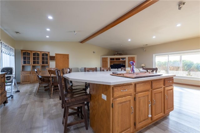 kitchen featuring hardwood / wood-style flooring, a breakfast bar area, lofted ceiling with beams, and a center island