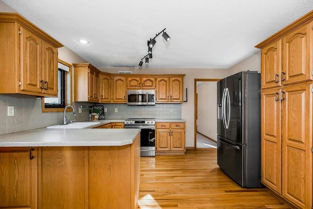 kitchen featuring kitchen peninsula, light hardwood / wood-style flooring, sink, tasteful backsplash, and stainless steel appliances