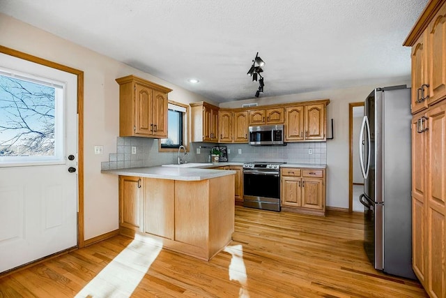 kitchen featuring kitchen peninsula, backsplash, light hardwood / wood-style floors, and stainless steel appliances