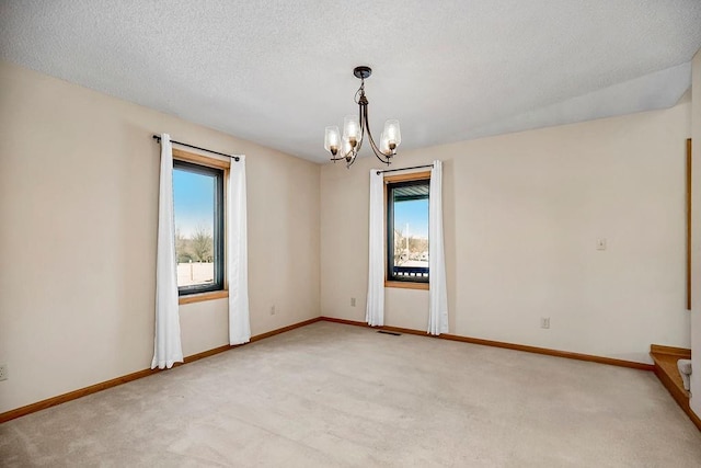 empty room featuring light colored carpet, an inviting chandelier, and a textured ceiling