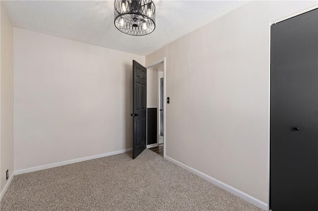 carpeted empty room with a textured ceiling and an inviting chandelier