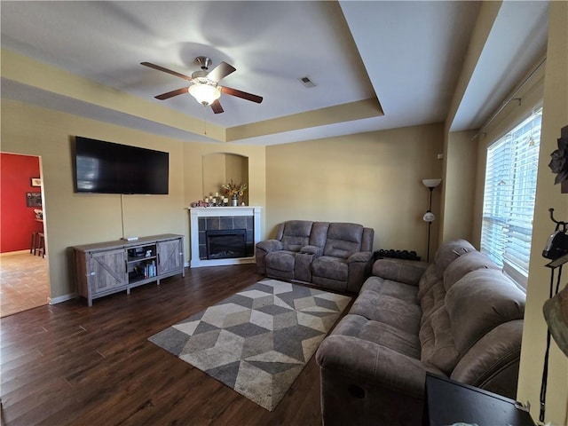 living room with ceiling fan, a tray ceiling, dark hardwood / wood-style floors, and a tiled fireplace