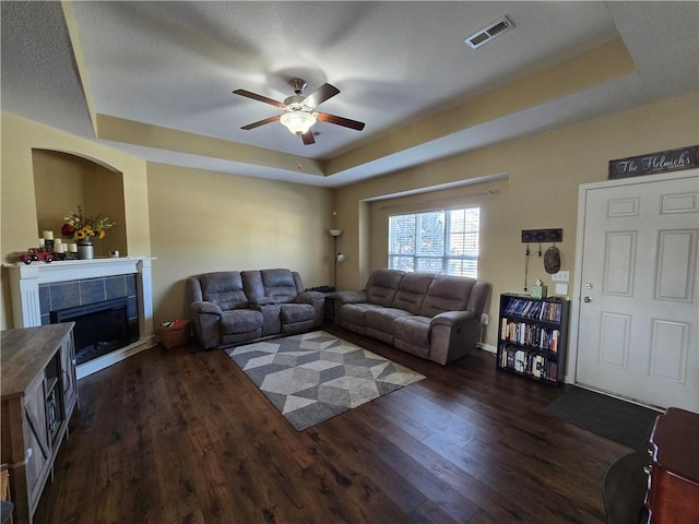 living room with a tiled fireplace, dark hardwood / wood-style floors, and a tray ceiling