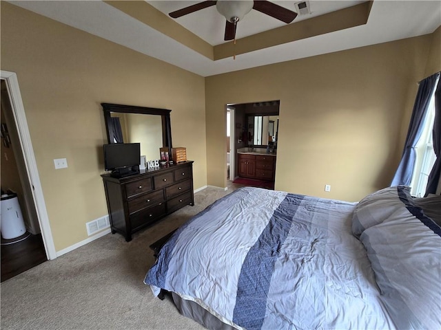 carpeted bedroom with ceiling fan, ensuite bathroom, and a tray ceiling