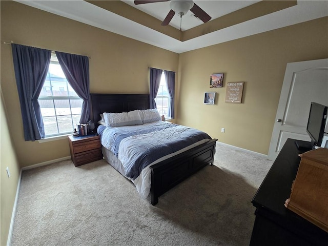 bedroom featuring multiple windows, light colored carpet, a raised ceiling, and ceiling fan