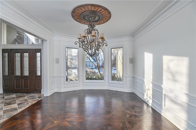 foyer featuring a notable chandelier, ornamental molding, and dark parquet floors