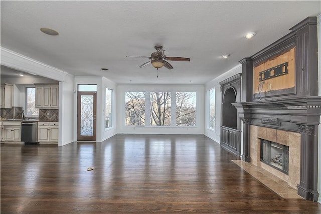 unfurnished living room with crown molding, a tile fireplace, dark hardwood / wood-style floors, and ceiling fan