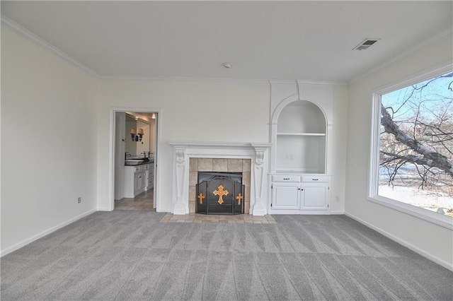 unfurnished living room featuring a healthy amount of sunlight, ornamental molding, a tiled fireplace, and light carpet