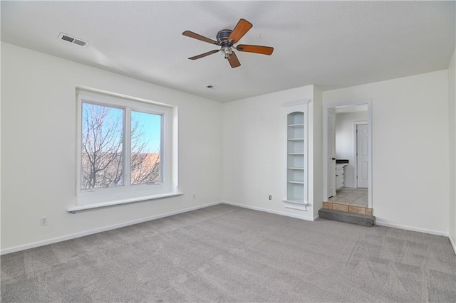 unfurnished room with ceiling fan, light colored carpet, and built in features