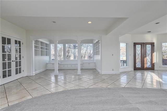 foyer entrance with decorative columns, a healthy amount of sunlight, light tile patterned floors, and french doors