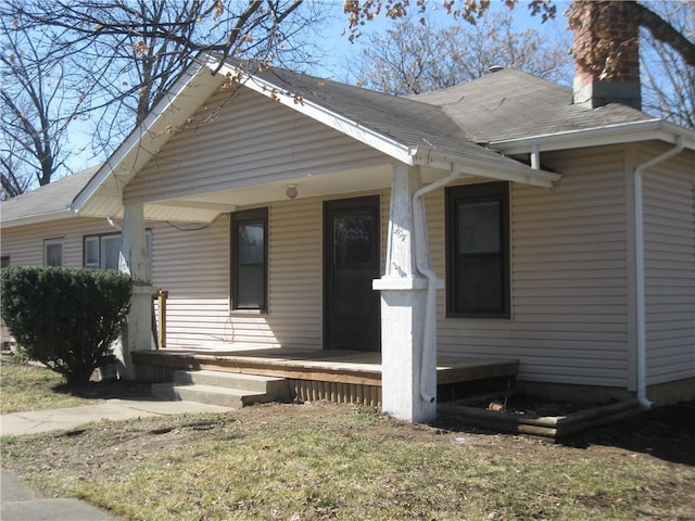 view of front facade featuring a porch, a chimney, and a shingled roof