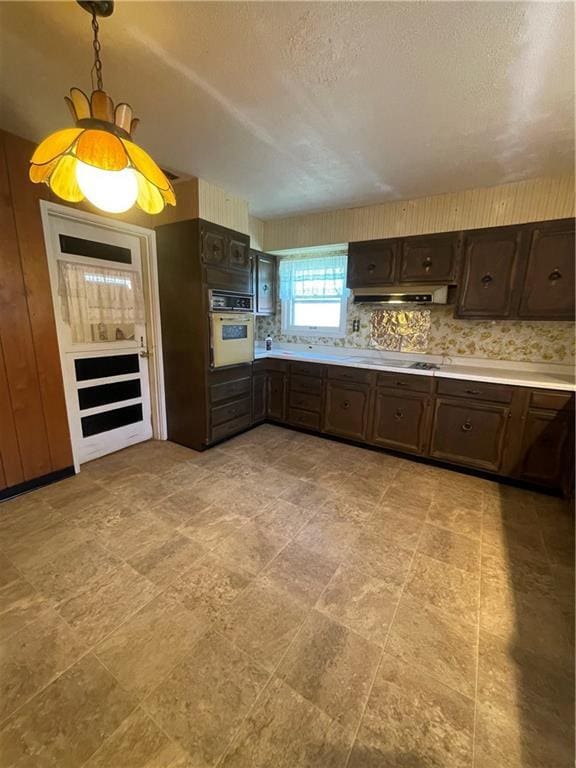 kitchen with decorative light fixtures, under cabinet range hood, dark brown cabinetry, light countertops, and white oven