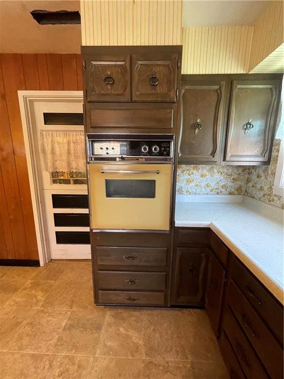 kitchen with wooden walls, dark brown cabinets, light countertops, and oven