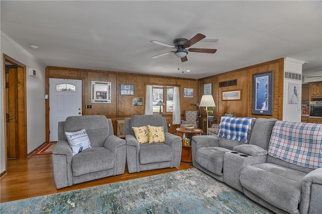 living room featuring hardwood / wood-style flooring, ornamental molding, ceiling fan, and wood walls