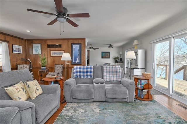 living room featuring wood-type flooring, ceiling fan, and wood walls