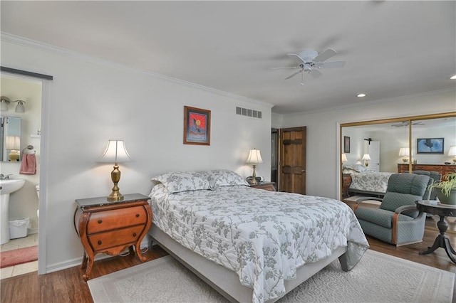 bedroom featuring ceiling fan, ensuite bathroom, wood-type flooring, ornamental molding, and a closet