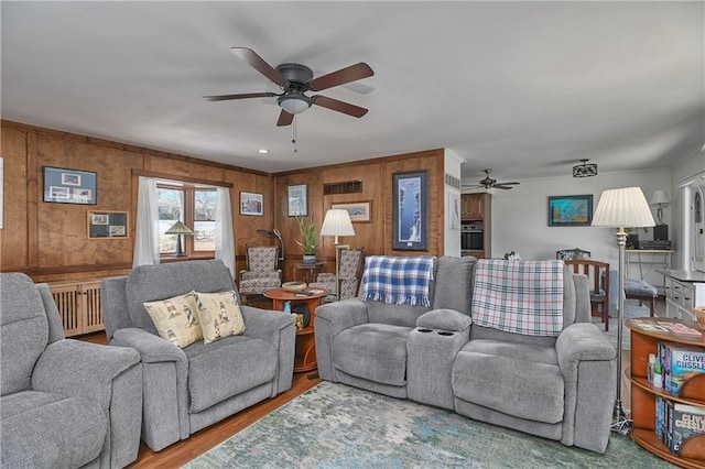 living area with wooden walls, wood finished floors, and ceiling fan