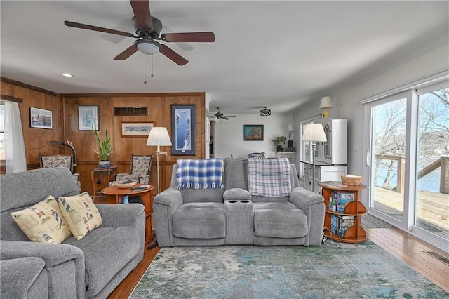 living room with hardwood / wood-style floors, visible vents, wood walls, and ceiling fan