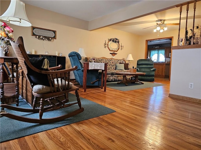 living area with a ceiling fan, wood finished floors, and beamed ceiling