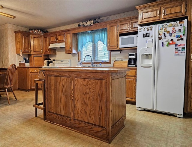 kitchen featuring white appliances, under cabinet range hood, light floors, and a center island with sink