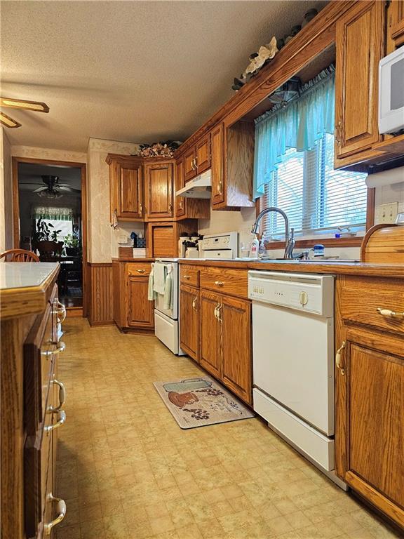 kitchen with brown cabinetry, white appliances, under cabinet range hood, and light floors