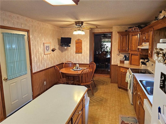 kitchen featuring range hood, a wainscoted wall, a textured ceiling, white appliances, and wallpapered walls