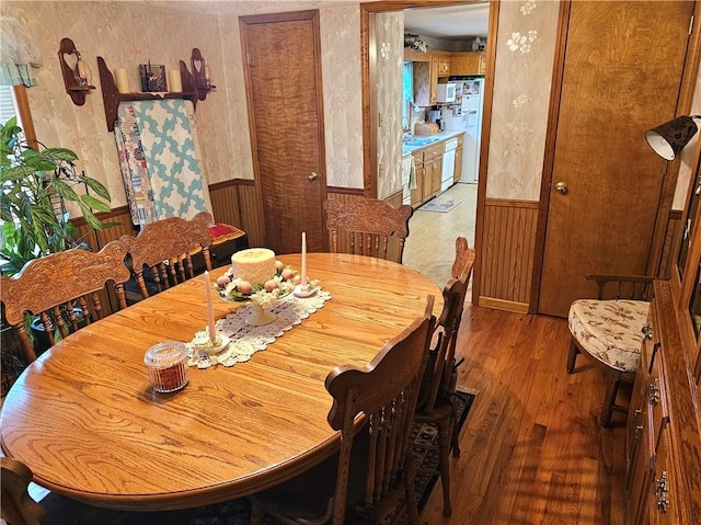 dining space with wallpapered walls, a wainscoted wall, and wood finished floors