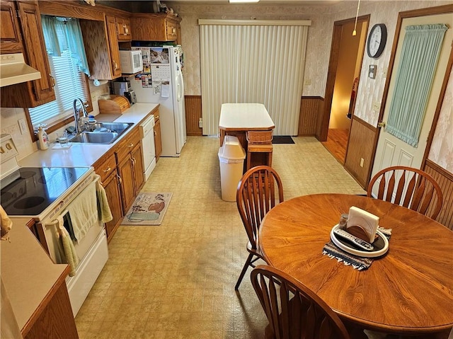 kitchen featuring a wainscoted wall, light floors, ventilation hood, white appliances, and wallpapered walls