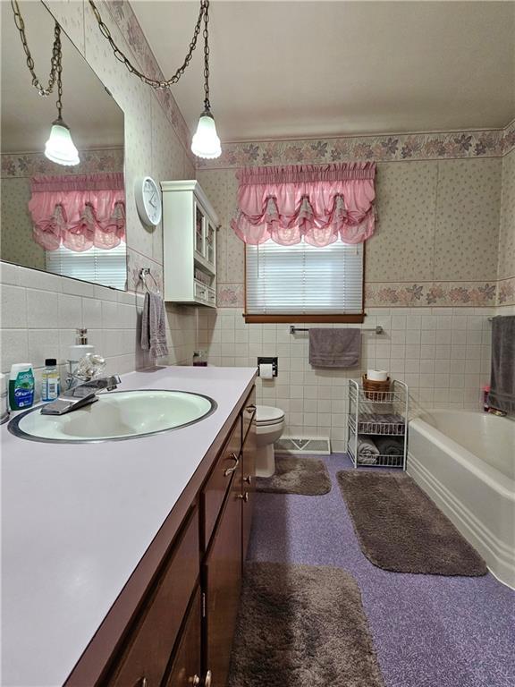 full bathroom featuring a bath, vanity, tile walls, and wallpapered walls