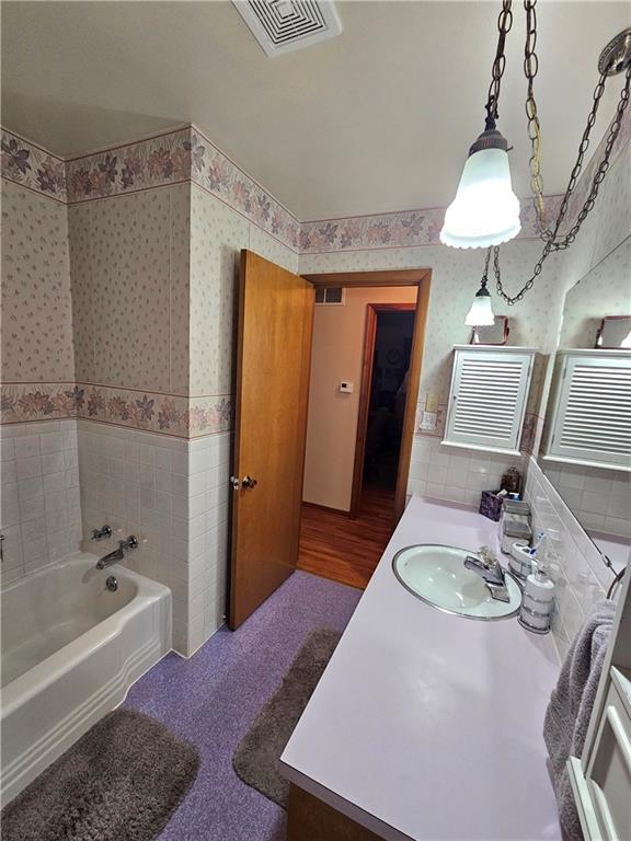 full bath with visible vents, tile walls, a bathing tub, and wallpapered walls