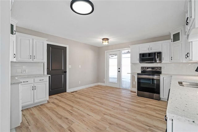 kitchen with stainless steel appliances, white cabinetry, light stone countertops, and backsplash