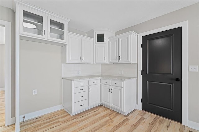 kitchen with light stone counters, light hardwood / wood-style floors, decorative backsplash, and white cabinets