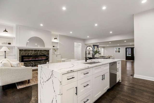 kitchen with white cabinetry, a kitchen island with sink, stainless steel dishwasher, light stone counters, and a premium fireplace