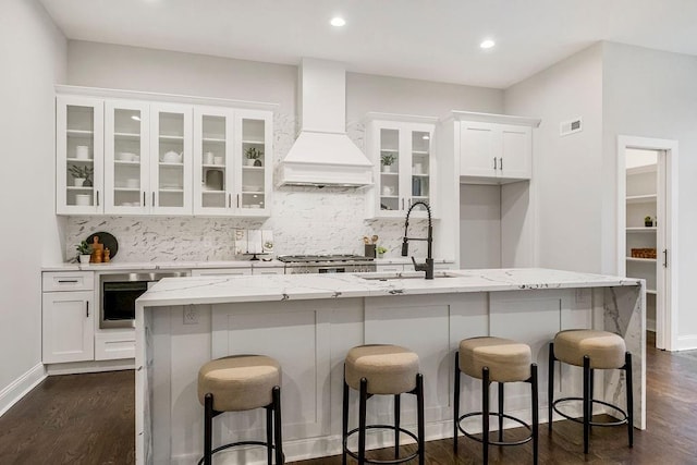 kitchen with white cabinetry, custom range hood, sink, and an island with sink