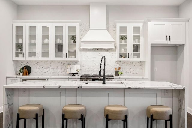 bar with white cabinetry, backsplash, light stone countertops, and premium range hood