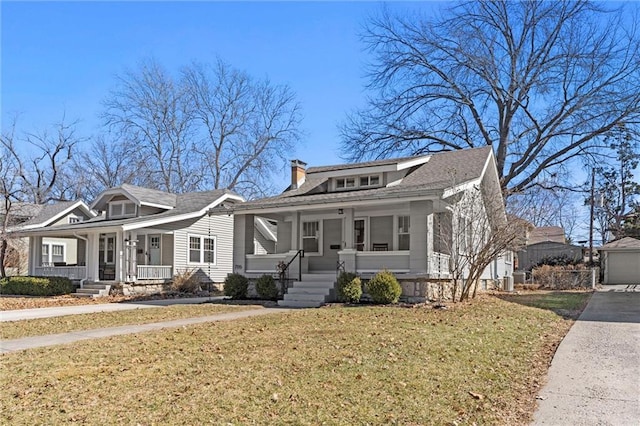 bungalow-style house with a porch, a front yard, a chimney, an outbuilding, and driveway