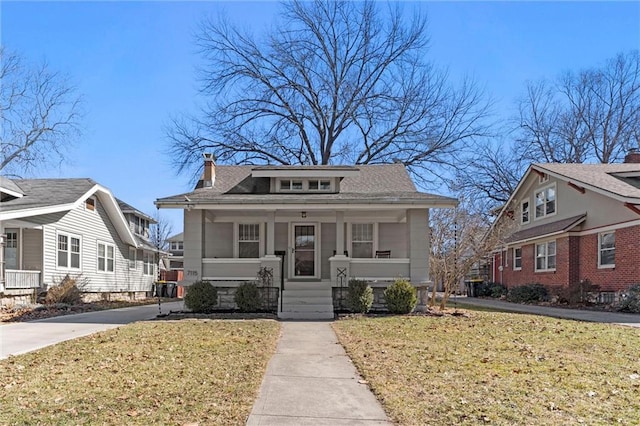 bungalow-style home featuring a porch, a chimney, a front yard, and roof with shingles