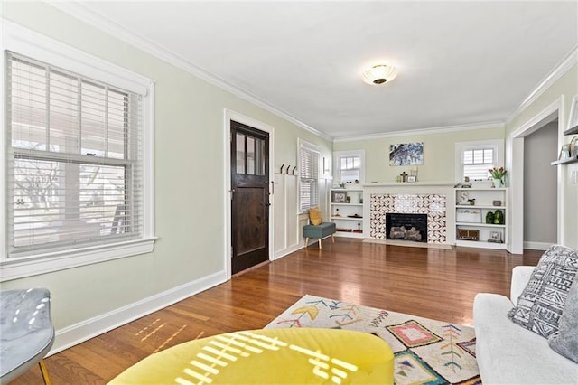 living area featuring a fireplace, wood finished floors, baseboards, and ornamental molding