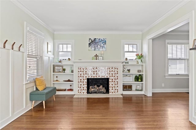 living room with plenty of natural light, wood finished floors, a tile fireplace, and ornamental molding