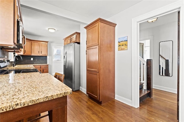 kitchen featuring light stone countertops, wood finished floors, baseboards, stainless steel appliances, and backsplash