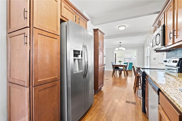 kitchen with visible vents, ornamental molding, stainless steel appliances, light wood-style floors, and light stone countertops