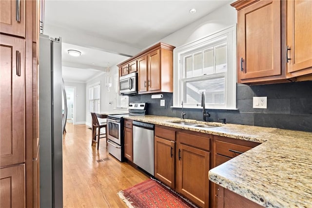 kitchen featuring a sink, decorative backsplash, stainless steel appliances, light wood-style floors, and brown cabinets